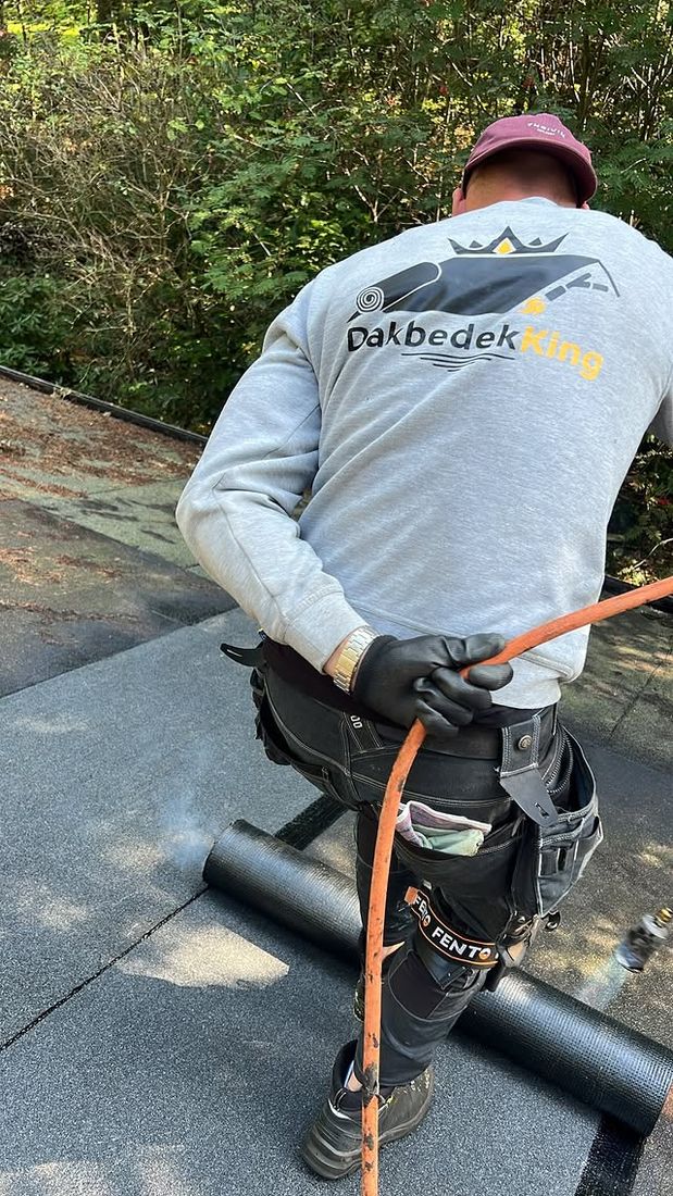 Een dakdekker van Dakbedek-King rolt een bitumen dakbaan uit op een plat dak.